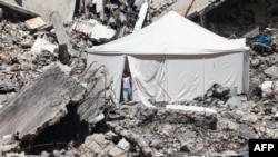 A displaced Palestinian stands at the entrance of a tent set up amid the rubble of a building damaged during Israeli bombardment in Rafah, on the southern Gaza Strip.